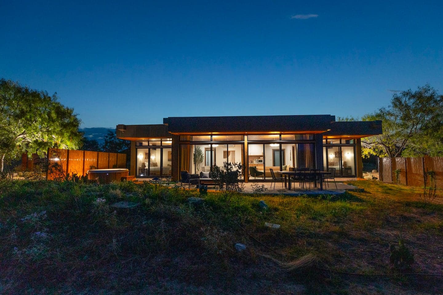 Modern Villa lit at twilight, glass walls open to the patio and hot tub